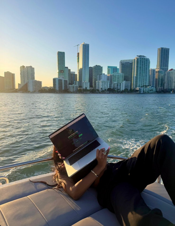 Monrae Hou working on a laptop with the Miami skyline at sunset